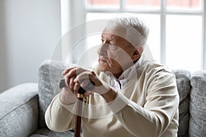 Pensive older man holding cane giving rest to tired feet
