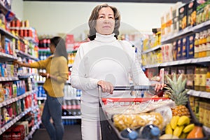 Pensive older woman walking with shopping cart at store