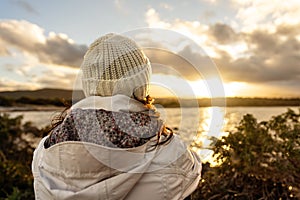 Pensive person view from back looking at the horizon. Unrecognizable woman seen from behind dressed in winter wool hooded clothes