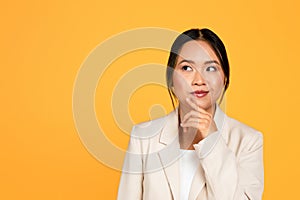 Pensive positive young asian woman in suit thinks, looking at empty space