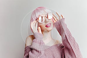 Pensive pretty girl in pink periwig looking up on light background. Indoor photo of short-haired stylish woman in purple