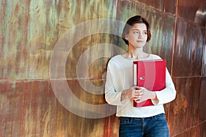 Pensive pretty young woman holding red ring binder folder