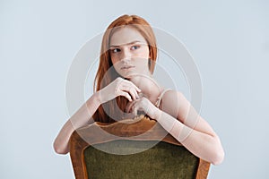 Pensive redhead woman sitting on the chair and looking away