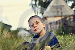 Pensive and sad look of a child with cerebral palsy. Summer evening boy sitting in the grass and looking into the photo