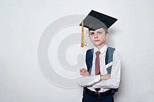 Pensive schoolboy wearing students hat and crossed his arms. Children education concept. White background, copy space