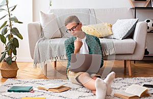 Pensive schooler making essay, looking at book, typing on laptop