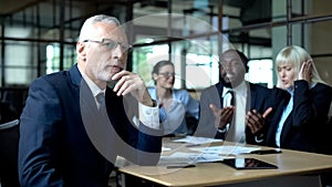Pensive senior businessman thinking, nervous colleagues arguing, stress at work