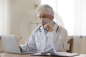Pensive senior male doctor think at workplace photo
