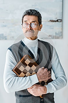 Pensive senior man holding chess board