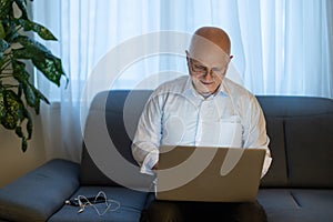 Pensive senior man reading news on laptop. Cheerful excited mature male using portable computer at home, copy space.