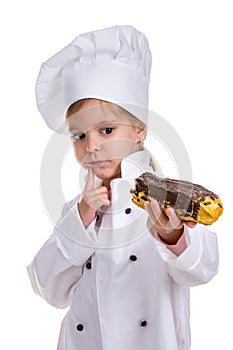 Pensive serious chef girl in a cap cook uniform, appraising the eclair. Looking at it. Portrait image
