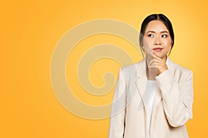 Pensive smart millennial japanese lady in suit thinks, looking at free space for ad and offer