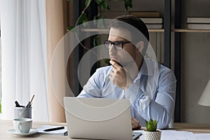 Pensive smart young businessman working on computer.