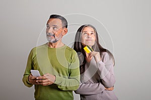 Pensive smiling caucasian elderly man with smartphone and lady with credit card dreaming about order