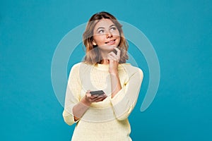 Pensive smiling woman in sweater holding smartphone and lookin up