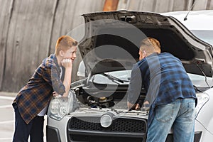 pensive son looking how father repairing car