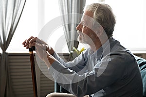 Pensive stressed middle aged disabled old man sitting on sofa.