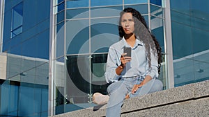 Pensive stressed sad upset worried woman girl with mobile phone sits in city near building thinks about problem looking