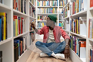 Pensive student african american man choosing research textbooks in university library.