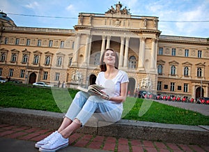 Pensive student girl with book on background of university