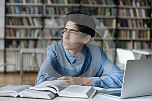 Pensive student guy staring aside, sit at table in library