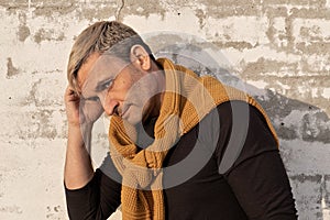 Pensive stylish charming blond middle-aged man of model appearance in front of a white brick wall. Handsome mature male model in