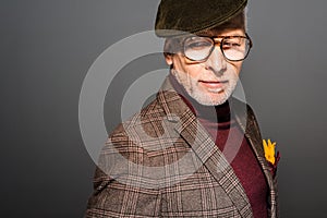 Pensive and stylish mature man in cap and glasses standing