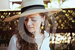 Pensive stylish woman in white shirt with hat in patio