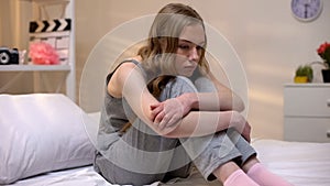 Pensive teen girl sitting alone in bedroom feeling abandoned, puberty depression