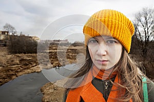 Pensive Teenager in orange knitten hat and scarf stand alone near the scorched field.