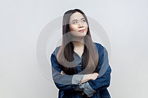 Pensive thoughtful brunette woman in blue denim jacket standing with crossed arms, thinking.