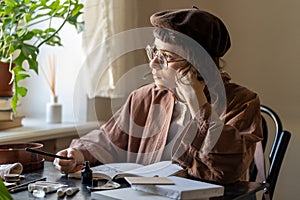 Pensive thoughtful female artist looking out window procrastinating while drawing in cozy art studio