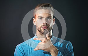 Pensive thoughtful unshaven man in denim shirt with hand on chin making decision feeling doubt. Serious bearded man