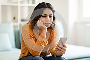 Pensive Upset Young Arab Woman Looking At Smartphone Screen At Home