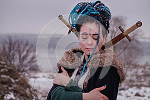 Pensive Viking woman with a sword in a black long mantle with fur. portrait of a dreamy girl with closed eyes. Female with blue