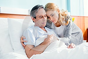 Pensive wife visiting elderly husband in hospital