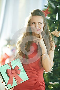 Pensive woman with green Christmas gift near Christmas tree