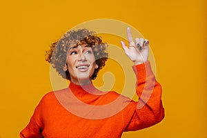 Pensive woman having an idea and pointing finger up isolated over yellow background