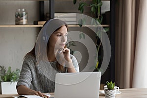 Pensive woman in headphones work on laptop thinking