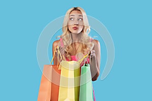 Pensive woman holding colorful shopping bags looking away