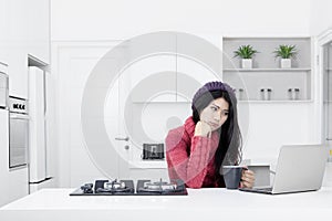 Pensive woman with a laptop in the kitchen
