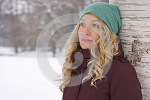 Pensive woman leaning against tree in winter