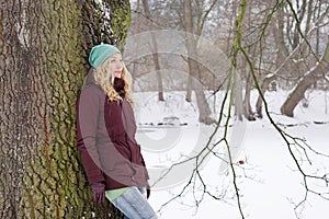 Pensive woman leaning against tree in winter