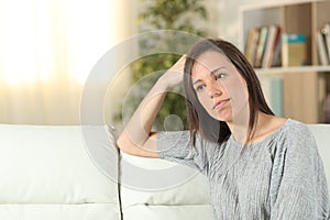 Pensive woman looking away on a couch at home