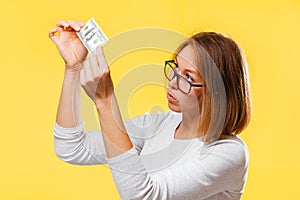 A pensive woman looking at the dollar bill checking for falsity. Yellow background. The concept of checking counterfeit photo