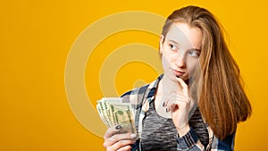 Pensive woman,  looking to the side, holding dollars,  received a scholarship, salary on a yellow background. Finance concept