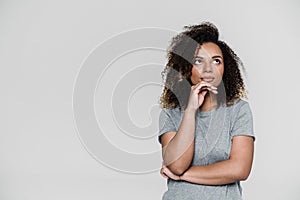 The pensive woman looking-up with hand propped on the chin while standing in the studio