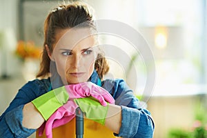 Pensive woman with mop at modern home in sunny day
