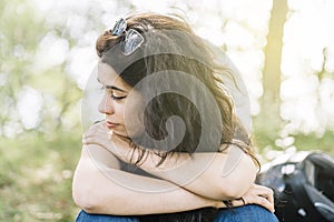 Pensive woman in nature sitting resting on her motorcycle route with her helmet behind