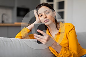 Pensive woman with phone looking sad and thoughtful on sofa